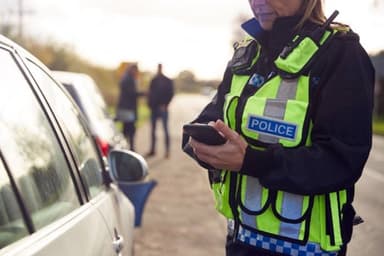 Police officer in high-visibility vest using a mobile device at a roadside, relevant to VAWG and RASSO policing work