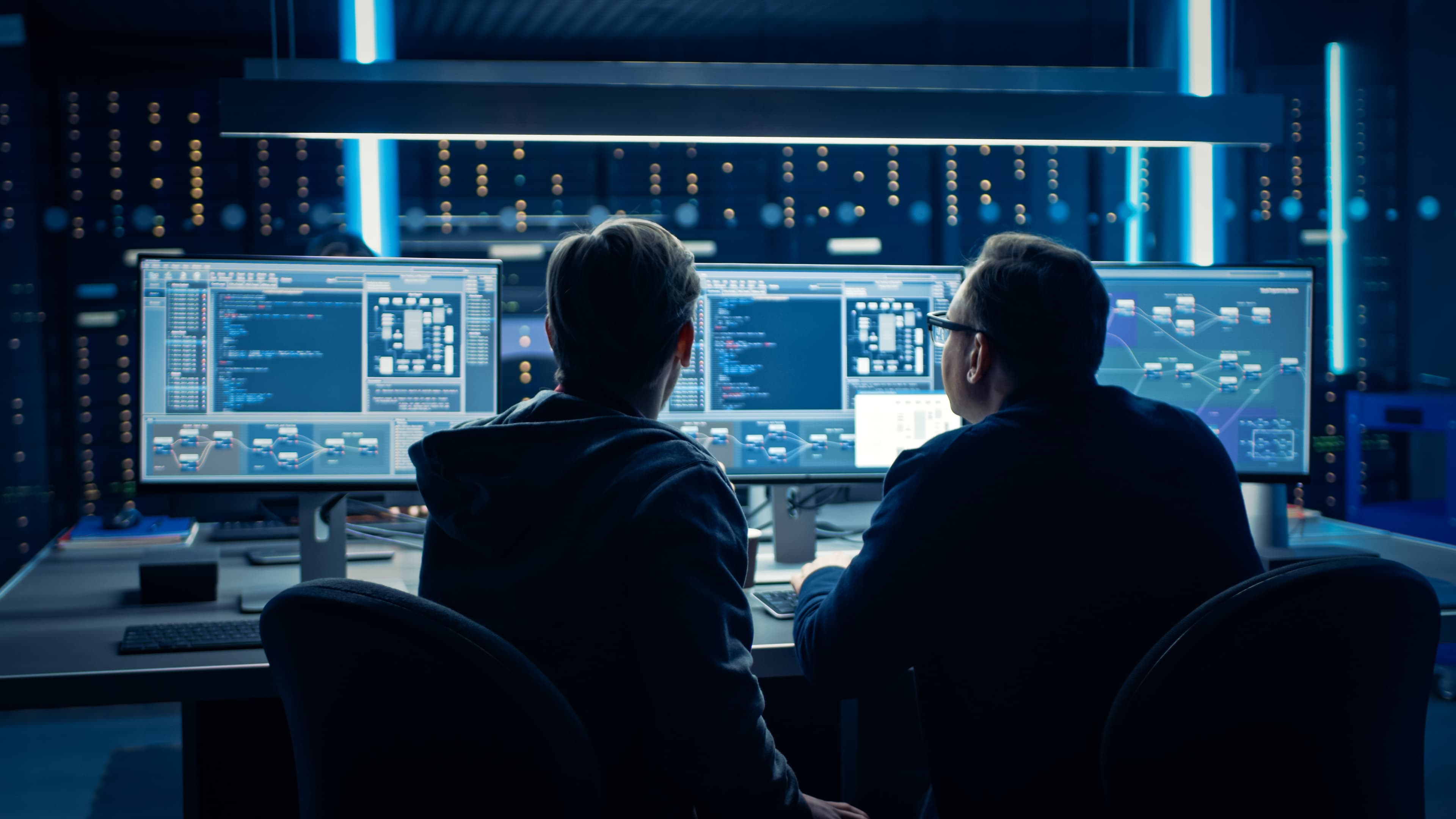 Two professionals viewing data and system information across multiple monitors